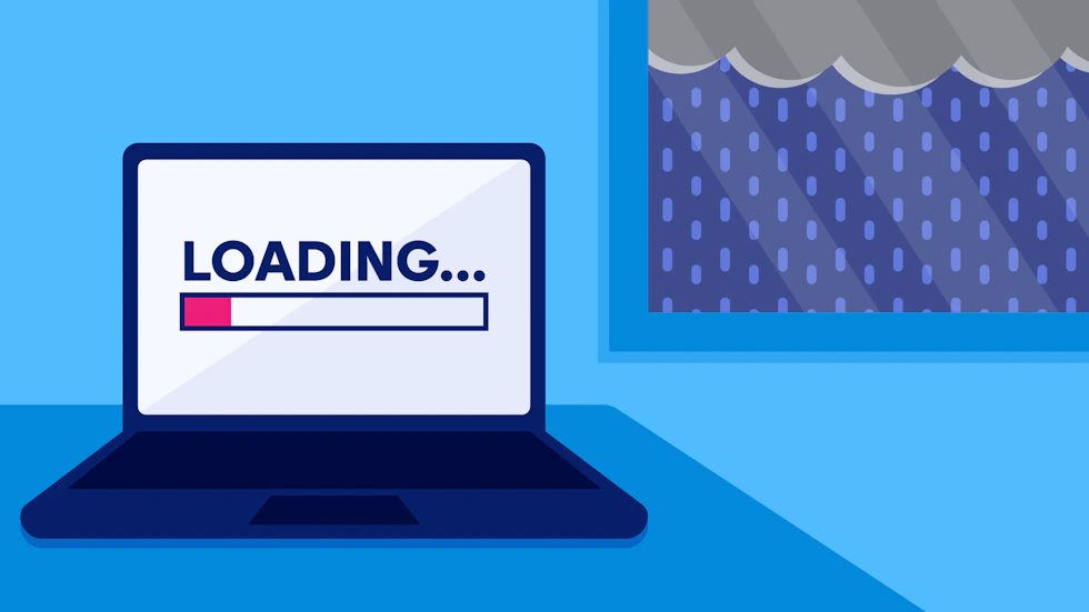 A laptop on a table with a loading screen next to a window that shows it's raining outside.